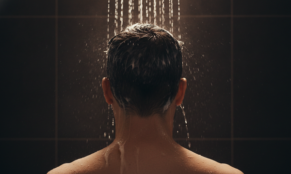 Achteraanzicht van een man die pomade uit zijn haar wast onder de douche